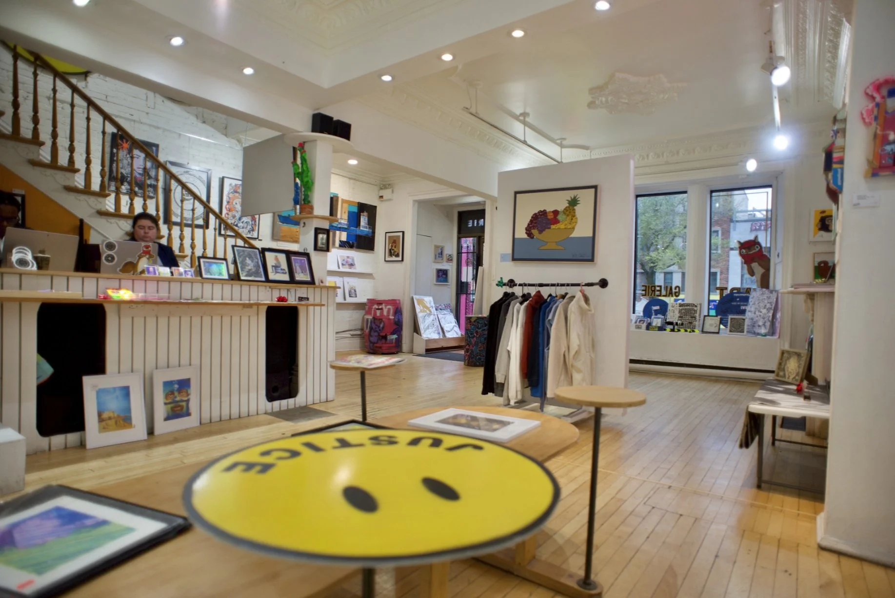 Intérieur lumineux de la galerie, avec des toiles et une table jaune au centre.