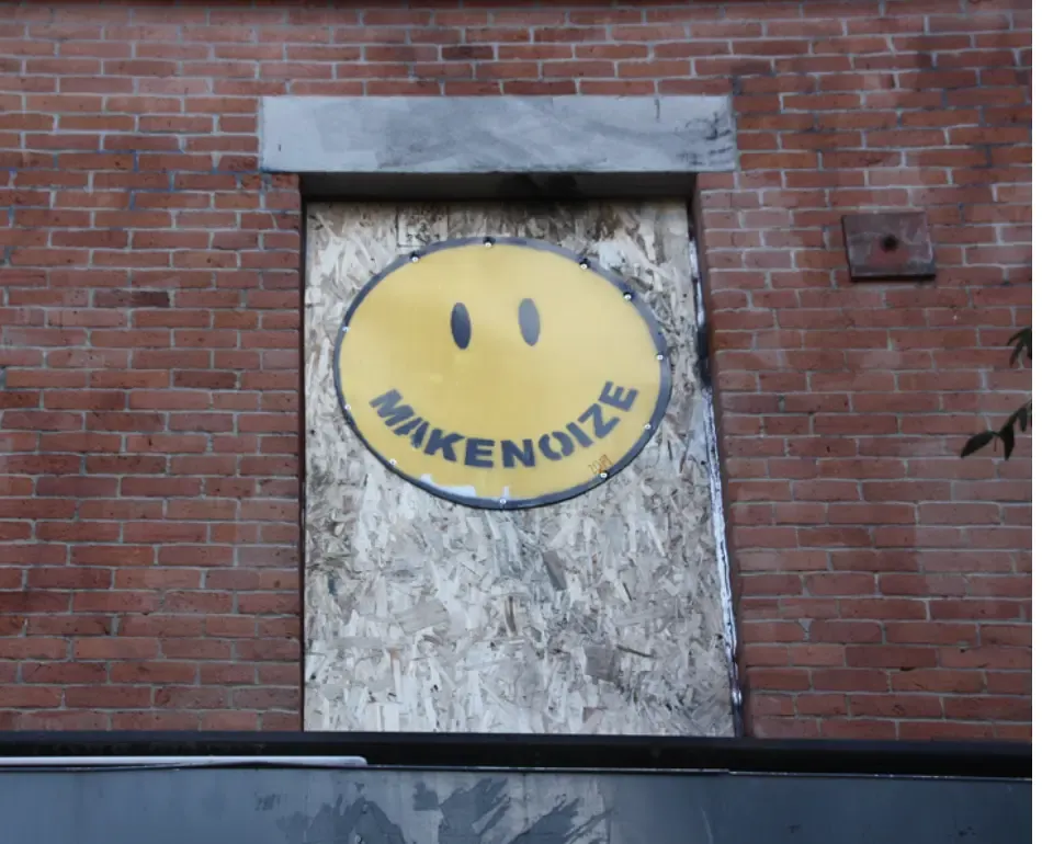 Le visage souriant de MakeNoize peint sur une fenêtre placardée.