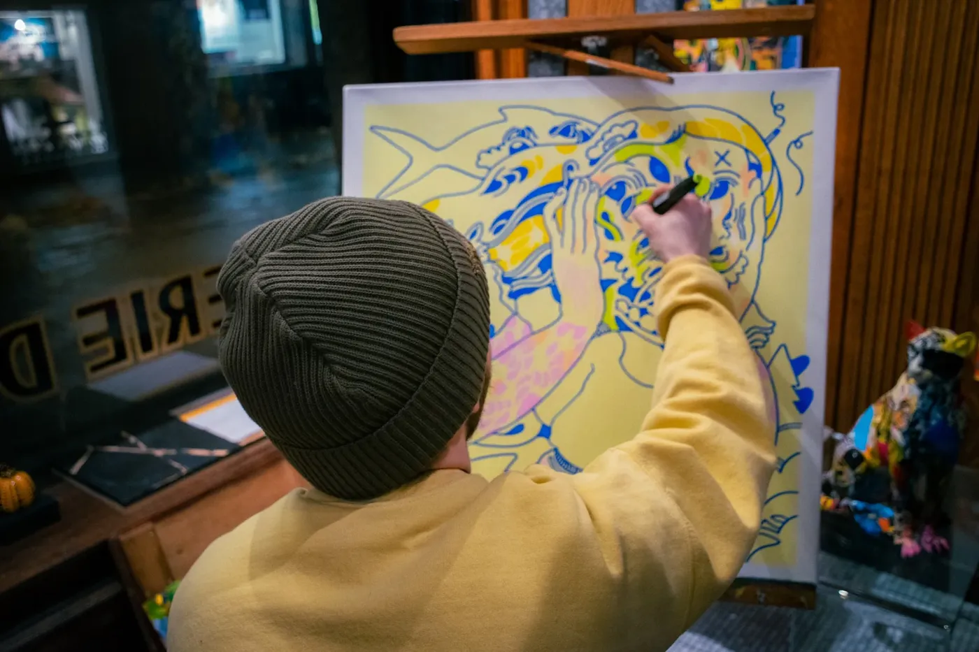 Un artiste dessine en direct sur une toile aux traits bleus et jaunes.