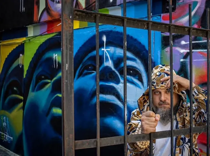Un homme derrière une grille devant une grande murale bleue.